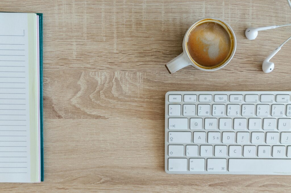 Anasayfa Flat lay of a workspace featuring coffee, a keyboard, and a notebook on a wooden desk.