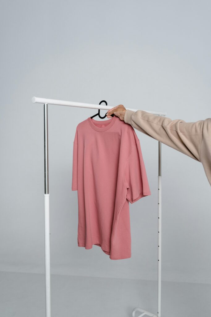 A pink t-shirt hangs on a rack held by a person, ideal for mockups and fashion design.
